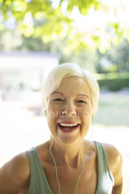 Portrait happy senior woman with headphones in sunny garden — Stock Photo