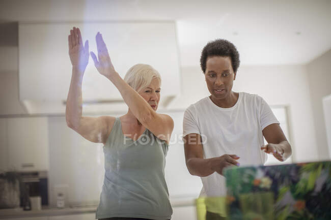 Las mujeres mayores amigos haciendo ejercicio en línea en el portátil en la cocina - foto de stock