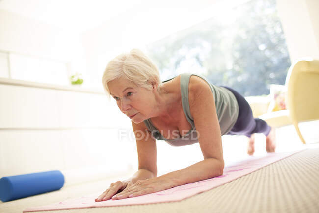 Femme âgée concentrée pratiquant l'exercice de planche sur tapis de yoga à la maison — Photo de stock