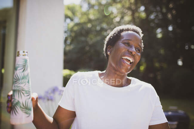 Щаслива зріла жінка з пляшкою води на сонячному літньому патіо — стокове фото
