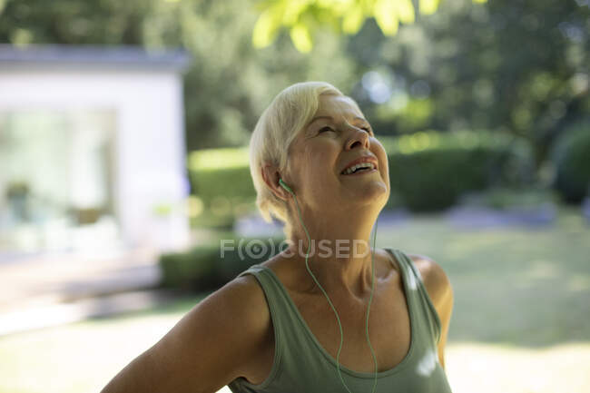 Mulher sênior feliz com fones de ouvido exercitando no jardim de verão — Fotografia de Stock