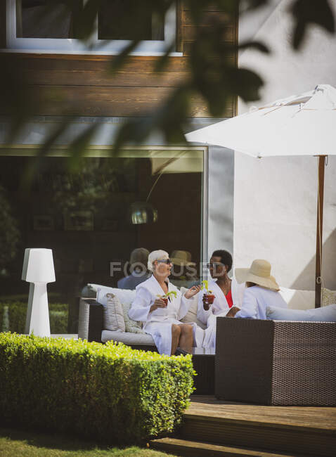 Donne anziane amiche che si rilassano in accappatoi spa sul patio soleggiato dell'hotel — Foto stock