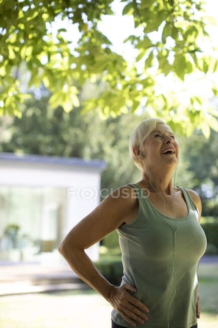 Щаслива старша жінка з навушниками вправляється в літньому саду — стокове фото