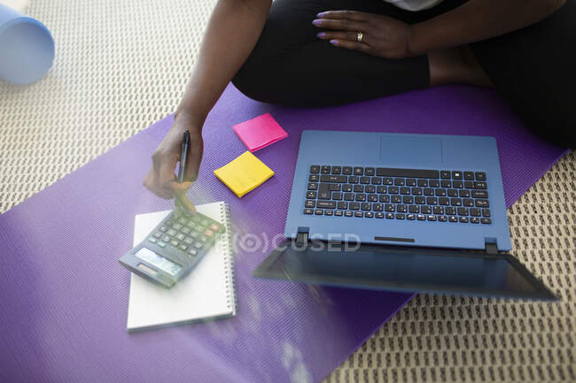 Donna che paga le bollette al computer portatile sul tappetino yoga a casa — Foto stock