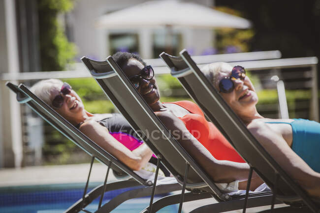 Retrato despreocupado mujeres mayores amigos tomando el sol en la piscina soleada - foto de stock
