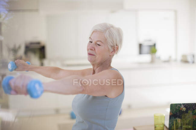 Старшая женщина упражняется с гантелями на кухне — стоковое фото