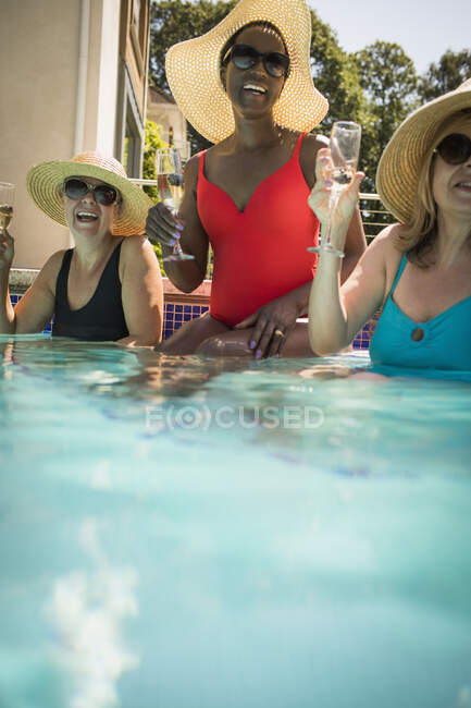 Felices amigas mayores bebiendo champán en la soleada piscina - foto de stock