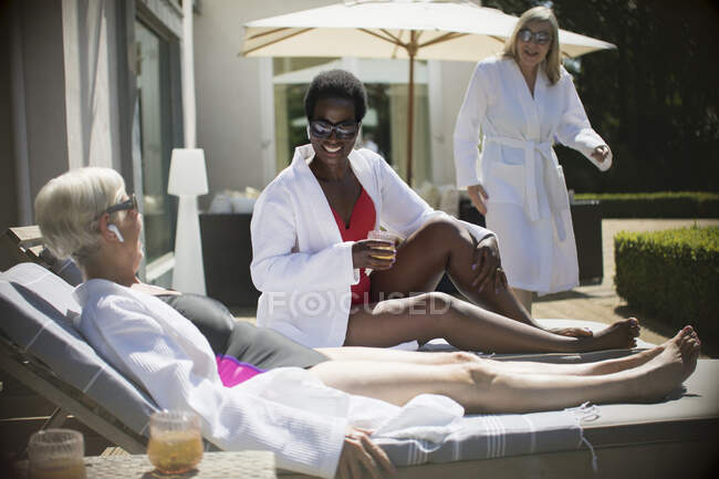 Heureuses femmes âgées amies relaxantes dans des peignoirs de spa sur le patio ensoleillé de l'hôtel — Photo de stock