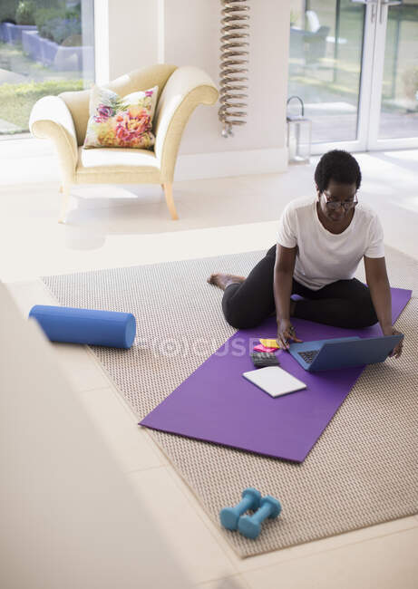Mature woman working at laptop on yoga mat at home — Stock Photo