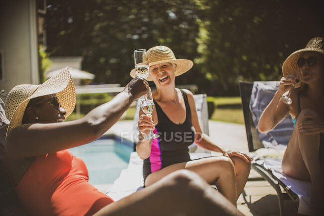 Glückliche Seniorinnen stoßen am sonnigen Pool mit Champagner an — Stockfoto