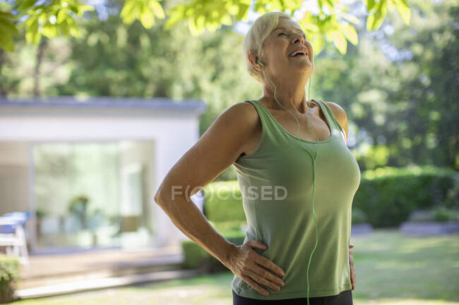 Carefree senior woman with headphones exercising in summer garden — Stock Photo