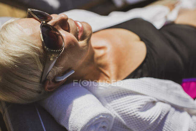 Feche a mulher sênior feliz em óculos de sol tomar banho de sol — Fotografia de Stock