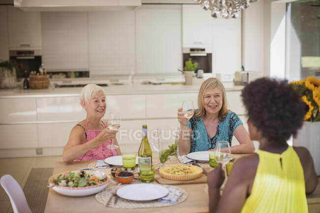 Друзі старших жінок насолоджуються білим вином з обідом за обіднім столом — стокове фото