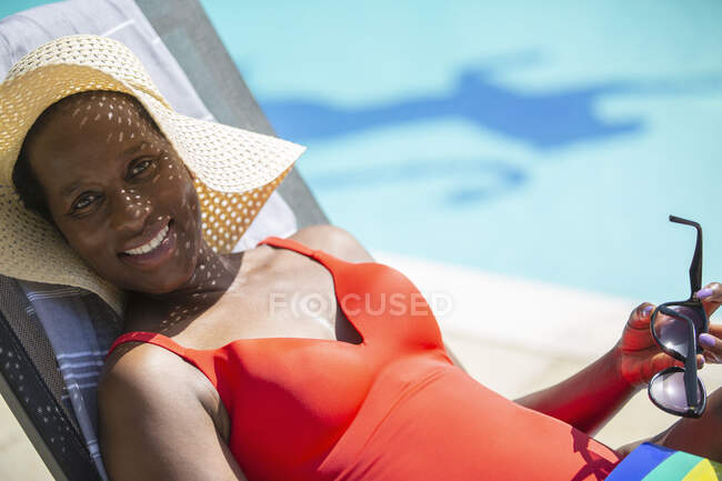 Portrait happy mature woman in sun hat sunbathing at sunny poolside — Stock Photo