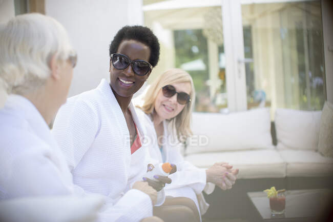 Donne anziane amiche con occhiali da sole e accappatoi termali sul patio dell'hotel — Foto stock