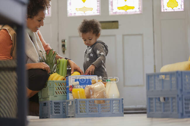 Curiosa hija bebé viendo madre desempacar caja de comestibles - foto de stock