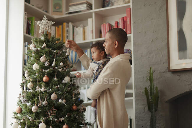 Padre e hija bebé decorando el árbol de Navidad en la sala de estar - foto de stock