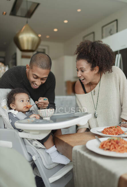 Casal feliz alimentando bebê filha em cadeira alta — Fotografia de Stock