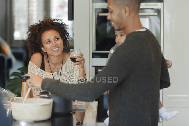 Glückliches Paar mit kleiner Tochter trinkt Wein und kocht Abendessen — Stockfoto