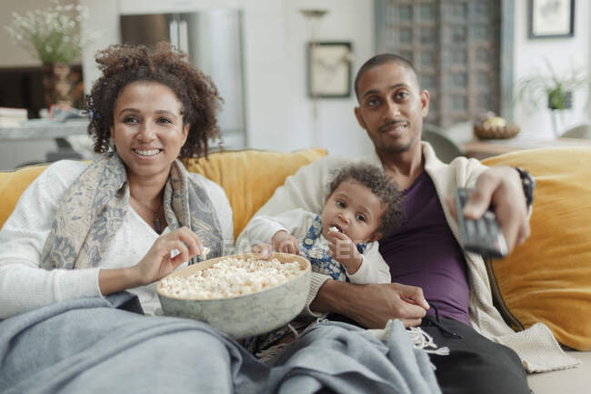 Happy couple with baby daughter watching TV and eating popcorn — Stock Photo