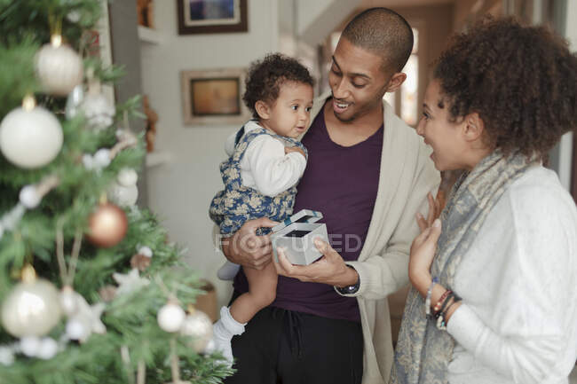 Happy parents and baby daughter opening Christmas gifts by tree — Stock Photo