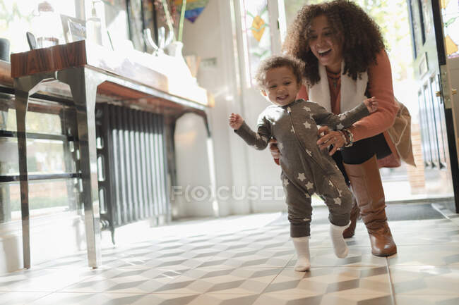 Mère heureuse aidant bébé fille apprendre à marcher à la maison — Photo de stock