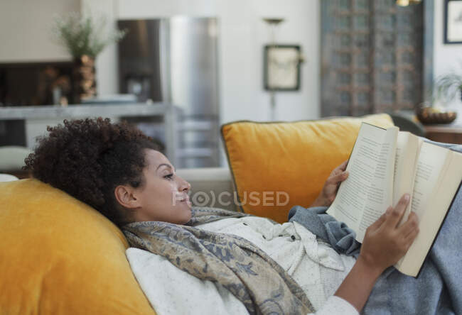 Serene livre de lecture femme sur canapé salon — Photo de stock
