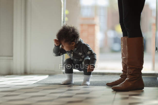 Cute baby girl in pajamas crouching at front door — Stock Photo