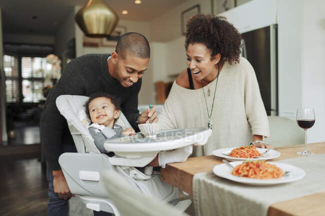Happy parents feeding baby daughter at dining table — Stock Photo