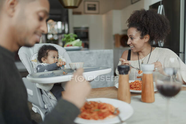 Pais felizes e bebê filha comer espaguete na mesa de jantar — Fotografia de Stock