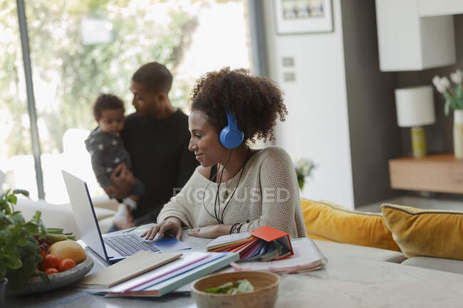 Woman working at laptop in dining room with husband and baby daughter — Stock Photo