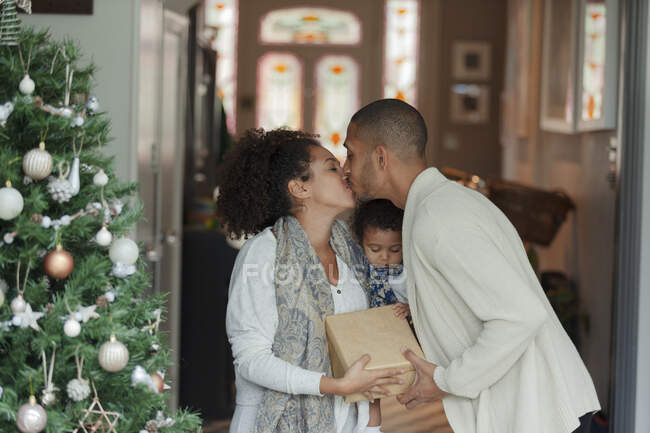 Pareja cariñosa con hija pequeña besándose en el árbol de Navidad - foto de stock