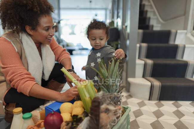 Cute baby daughter helping mother unpack grocery delivery — Stock Photo