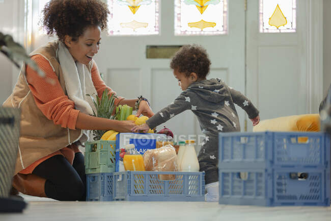 Baby daughter helping mother unload grocery delivery — Stock Photo