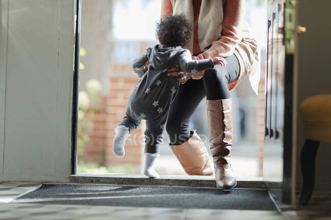 Mother lifting baby daughter in pajamas at front door — Stock Photo
