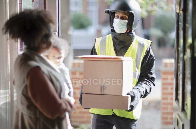 Woman receiving parcels from delivery man in face mask at front door — Stock Photo
