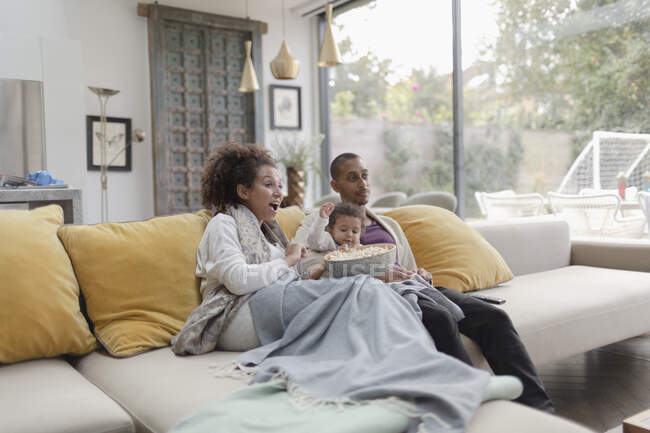 Семья смотрит кино и ест попкорн на диване в гостиной — стоковое фото