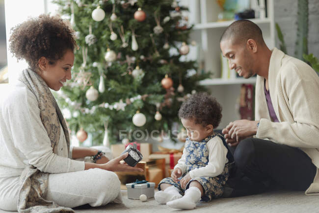 Батьки допомагають доньці відкрити різдвяні подарунки на дереві — стокове фото