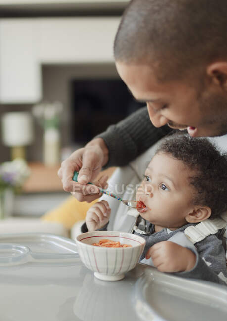 Father feeding cute baby daughter at high chair — Stock Photo