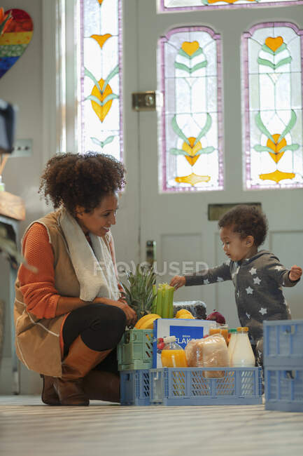 Bonito bebê filha ajudando mãe com mercearia entrega no foyer — Fotografia de Stock