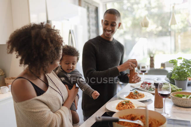 Genitori felici con la bambina che cucinano spaghetti in cucina — Foto stock