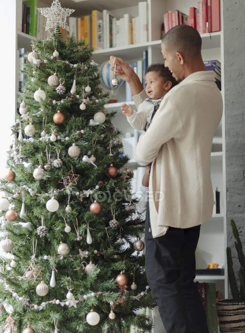 Padre e hija bebé decorando el árbol de Navidad en la sala de estar - foto de stock