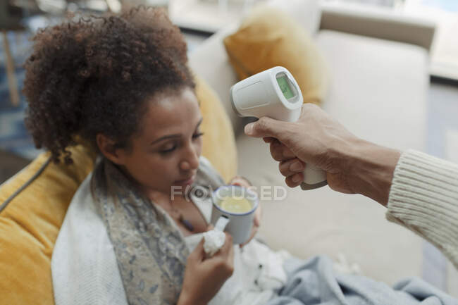 Чоловік приймає температуру хворої дружини з інфрачервоним термометром — стокове фото