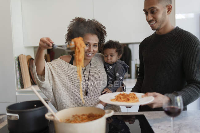 Parents with baby daughter cooking spaghetti at kitchen stove — Stock Photo