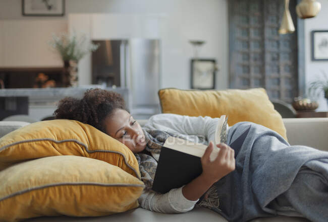 Woman relaxing and reading book on living room sofa — Stock Photo