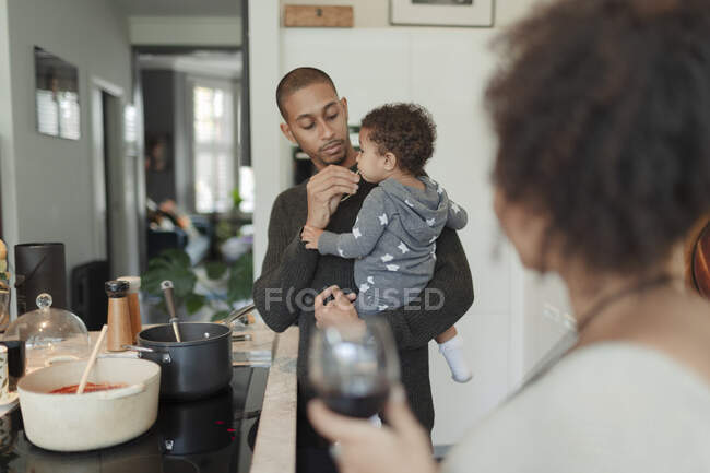 Pai segurando bebê filha e cozinhar jantar no fogão da cozinha — Fotografia de Stock