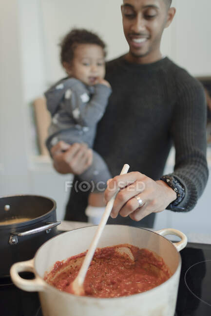 Father holding baby daughter and cooking spaghetti at stove — Stock Photo