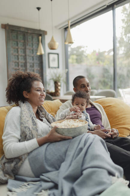 Family watching movie and eating popcorn on living room sofa — Stock Photo