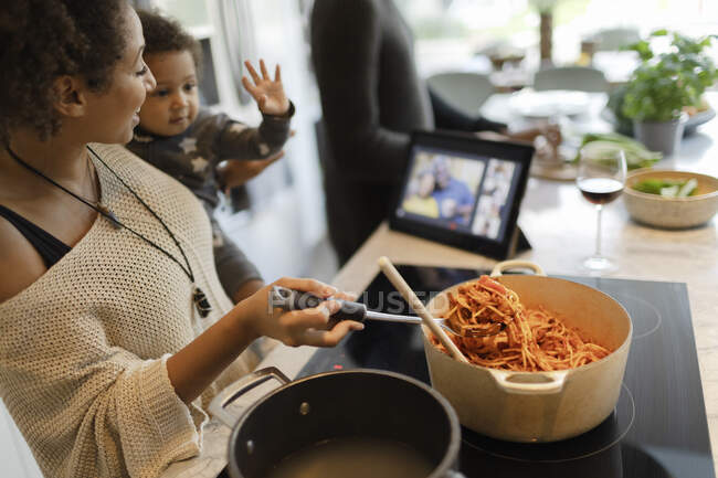 Mãe e bebê filha cozinhar espaguete e vídeo bate-papo — Fotografia de Stock