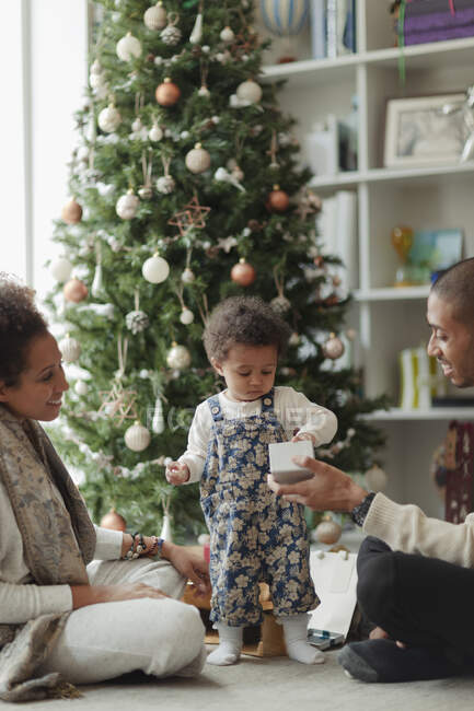 Casal ajudando bebê filha abrir presente de Natal na sala de estar — Fotografia de Stock